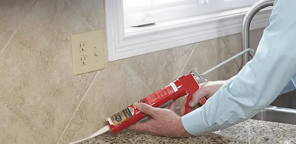 Handyman applying caulk along a kitchen backsplash and countertop seam in Oklahoma City, OK